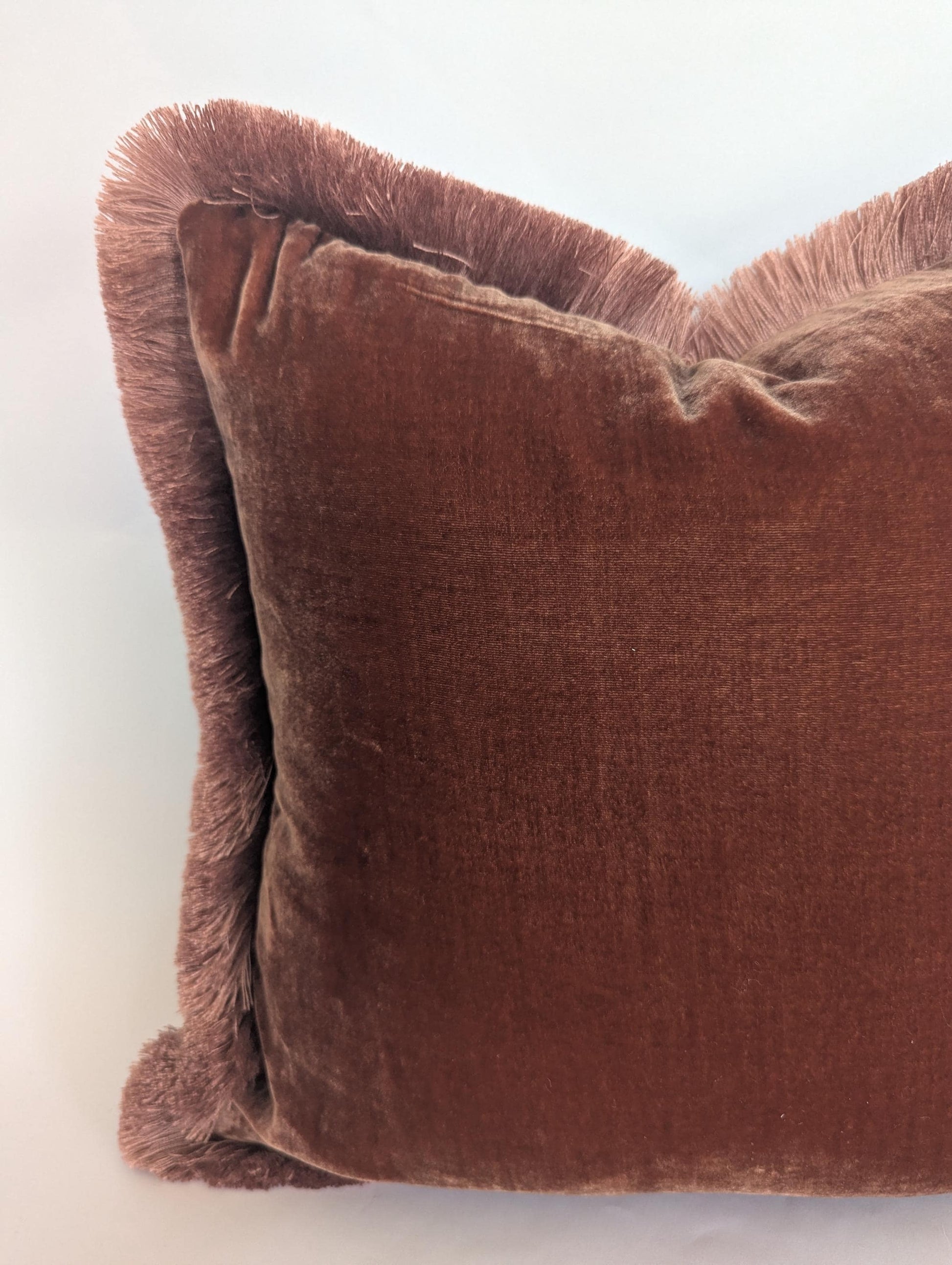 May include: A rectangular cushion in a dusty rose velvet with a fringe trim. The soft, plush cushion has a fringe border in a lighter rose hue. This home decor item is designed to add a touch of elegance. The cushion is a home decor item.